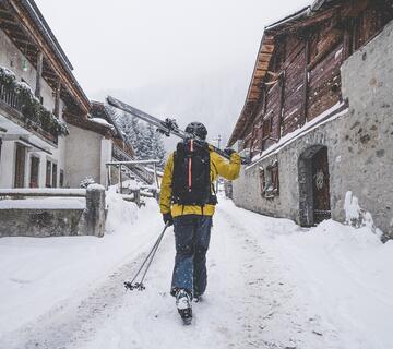 Skieuse qui marche dans une ruelle enneigée d'Argentière avec ses skis à la main