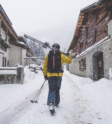 Skieuse qui marche dans une ruelle enneigée d'Argentière avec ses skis à la main