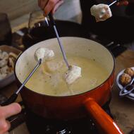 Casserole de fromage fondu dans laquelle des gens trempent des piques à fondue 
